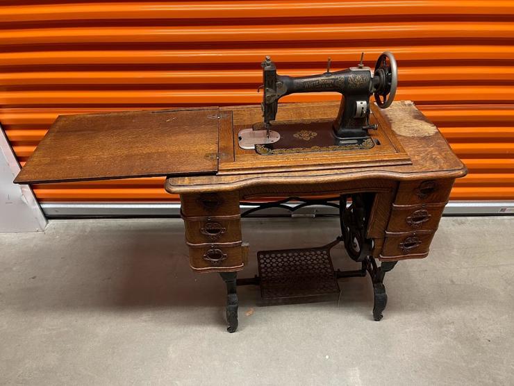 Vintage White sewing machine cabinet, with machine visible and sewing surface extended. There is some water damage on the surface of the cabinet. 