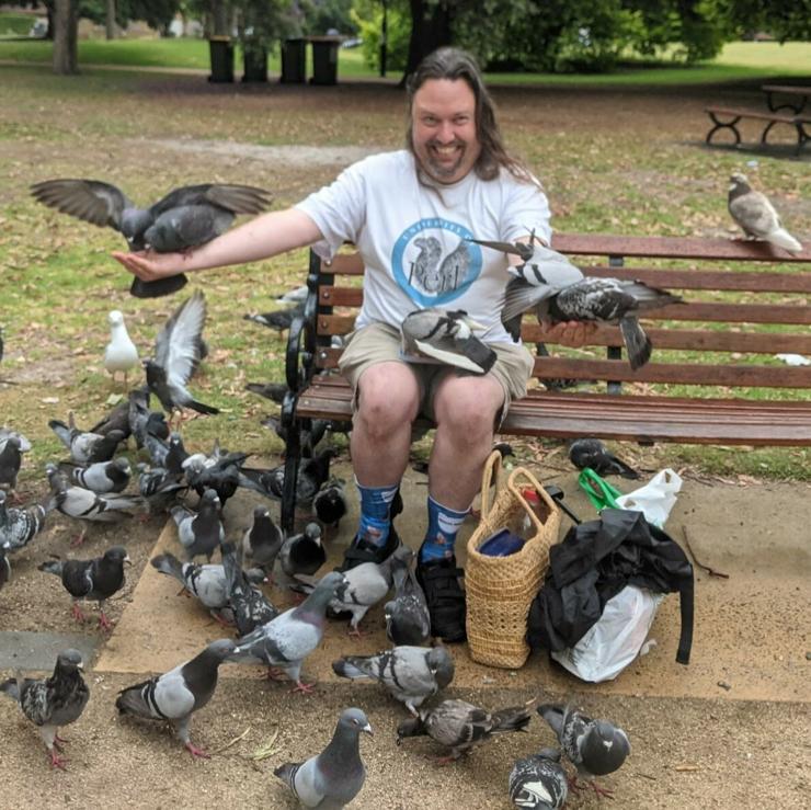 Me, sitting on a park bench, wearing a University of Perl t-shirt. I'm absolutely surrounded by and covered in pigeons. One of them is named Bobo and is very beautiful.